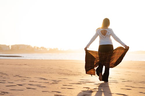 Woman Walking at the Beach While Holding a Scarf
