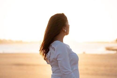 Free Woman in White Dress Shirt Standing on Brown Sand Stock Photo