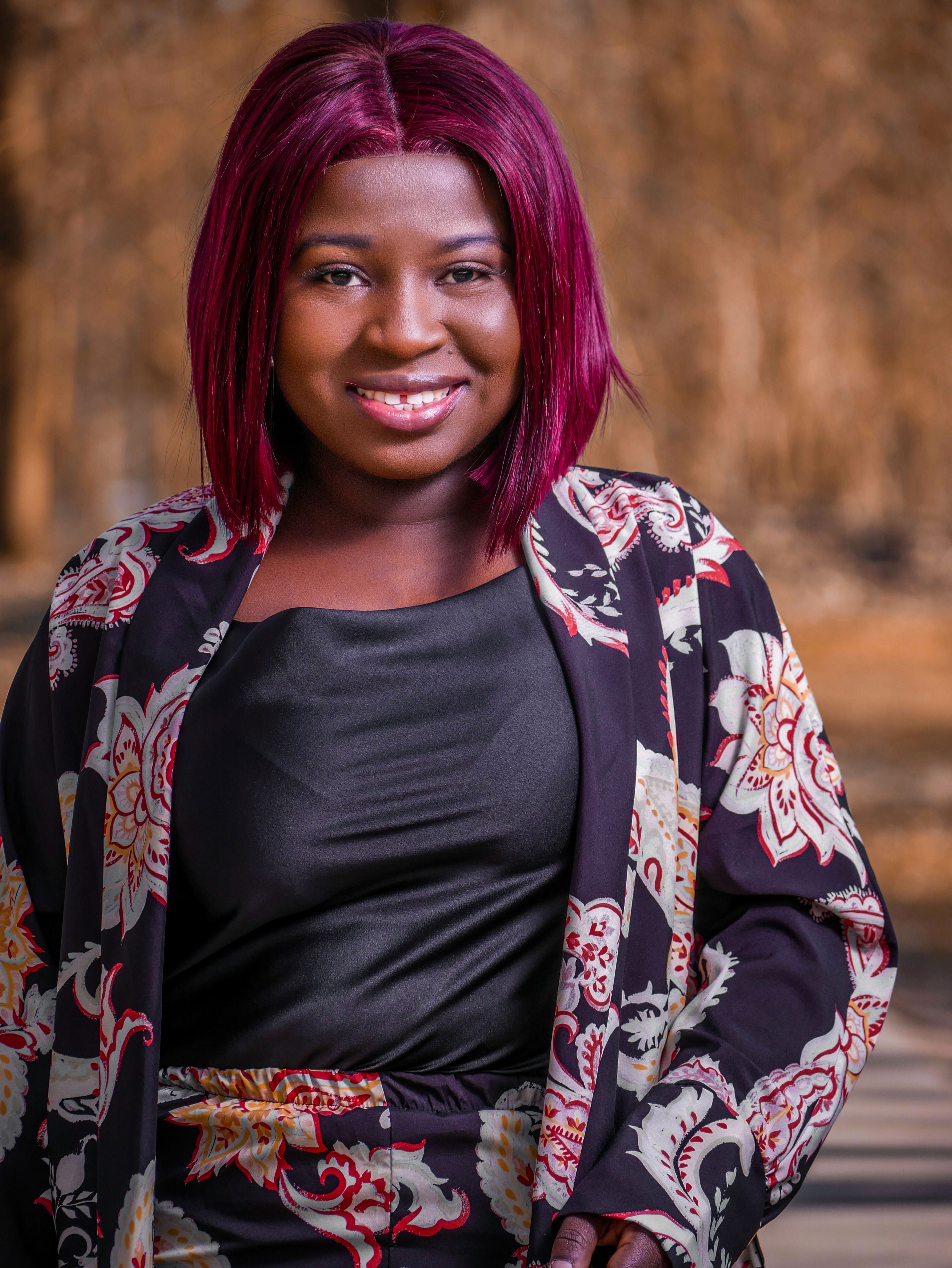 Portrait of a smiling woman with colored hair wearing floral attire outdoors.