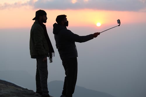 Silhouette of People doing Selfie on Mountain during Sunset