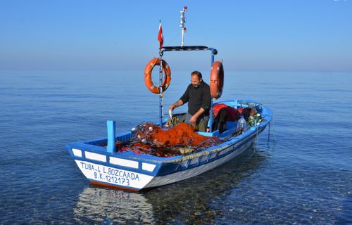 Free A fisherman on a traditional boat in Geyikli, Turkey, sorting fishing nets. Stock Photo