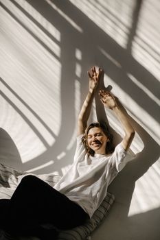 Smiling woman stretching with arms up in sunlight and shadows indoors.