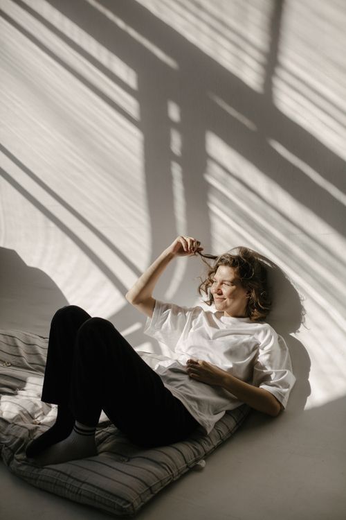Free A woman reclines on a cushion, enjoying the natural sunlight and artistic shadows. Stock Photo