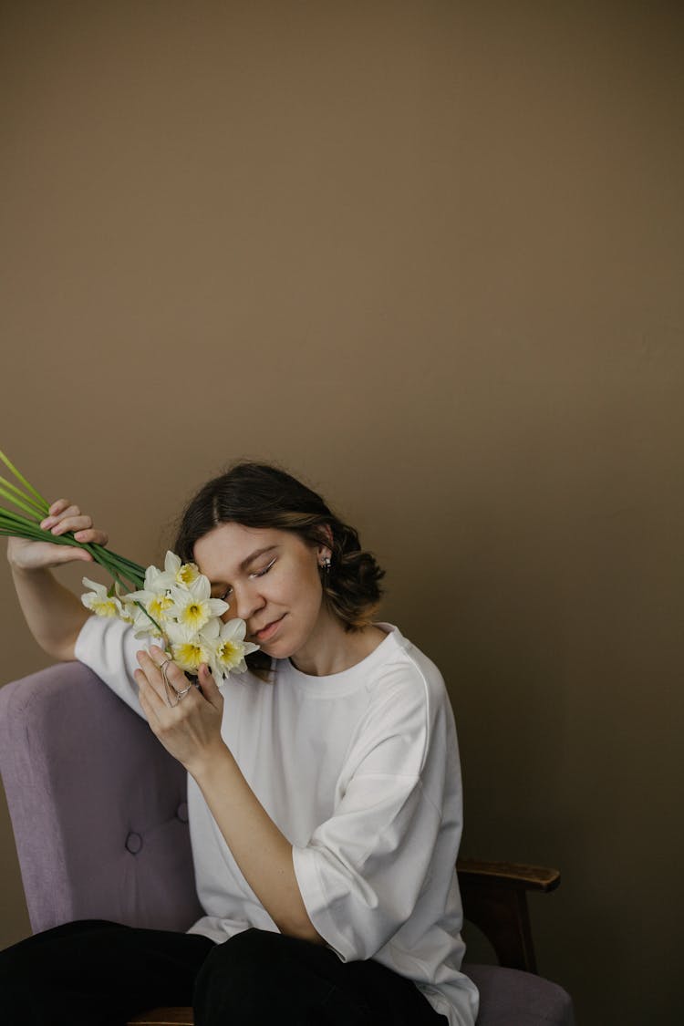 Woman Sitting And Holding Daffodils Next To Her Face