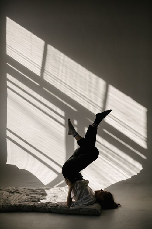 Free Person practicing yoga pose in a sunlit studio with dramatic shadows on the wall. Stock Photo