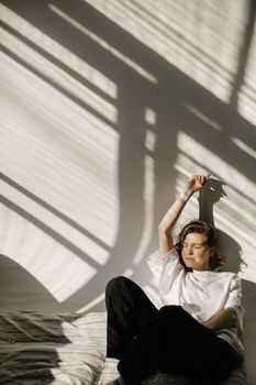 A woman sits and relaxes in a sunlit room with artistic shadows creating a serene atmosphere.