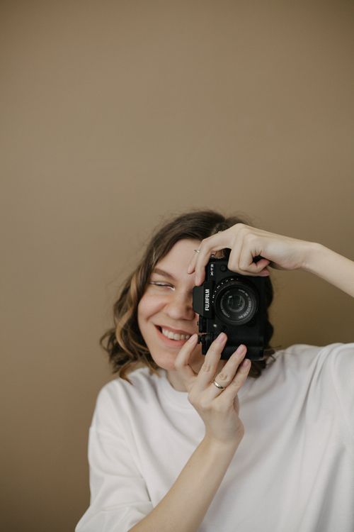 Free A smiling woman holding a camera against a neutral background. Stock Photo