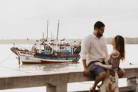 A loving couple sits by a calm lake with a fishing boat in the background, evoking romance and tranquility.