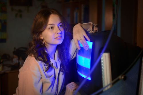 Free Young woman posing with a vintage CRT TV, illuminated by blue light indoors, creating a nostalgic ambiance. Stock Photo