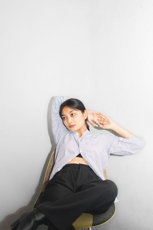 Free Asian woman in a stylish outfit sits relaxed indoors, showcasing modern style and elegance. Stock Photo