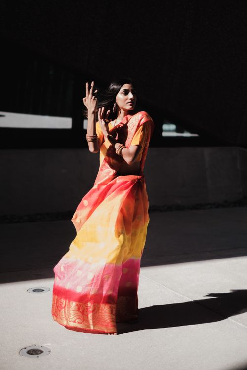 Free Model posing gracefully in a vibrant orange and pink saree, set against a dark modern backdrop. Stock Photo