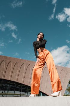 Low angle outdoor shot of a fashionable woman in orange pants against a blue sky in Orlando.