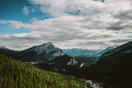 Breathtaking view of snow-covered mountains and lush forest under a dramatic sky.