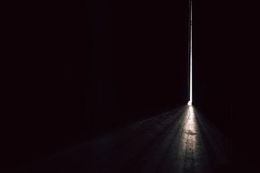 A narrow beam of light piercing through a dark room from a slightly open door.