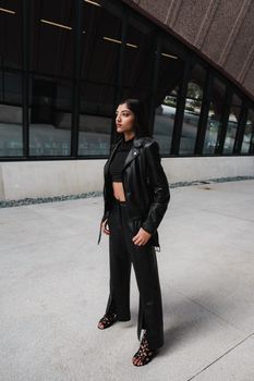 Stylish woman in black leather jacket and pants standing outside a modern building.