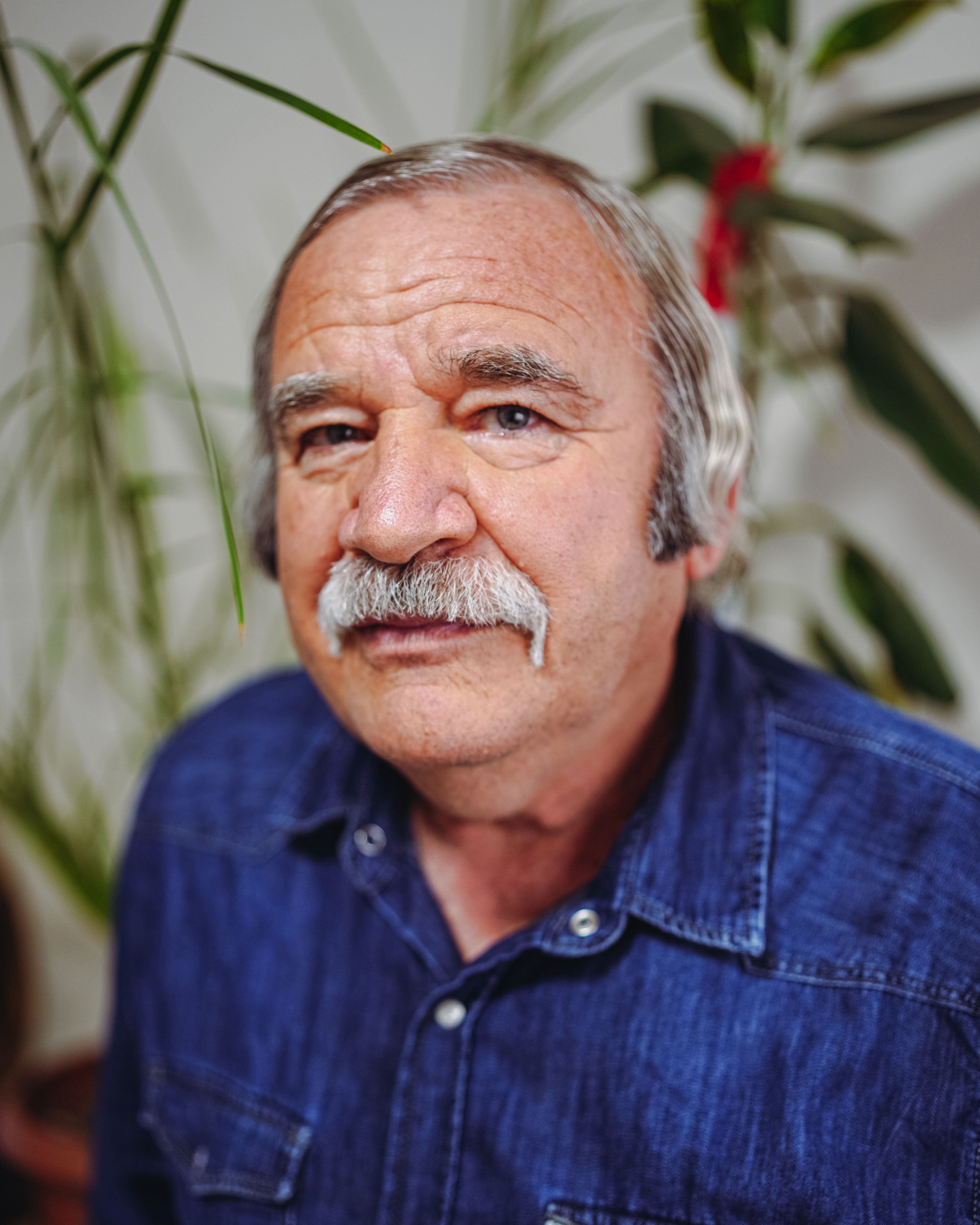 Close-up portrait of an elderly man with a mustache, set indoors.