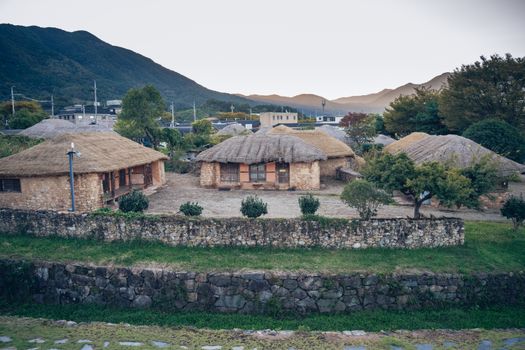 Rustic thatched huts nestled in a serene countryside setting with mountains in the background. - Fotografer Sidoarjo
