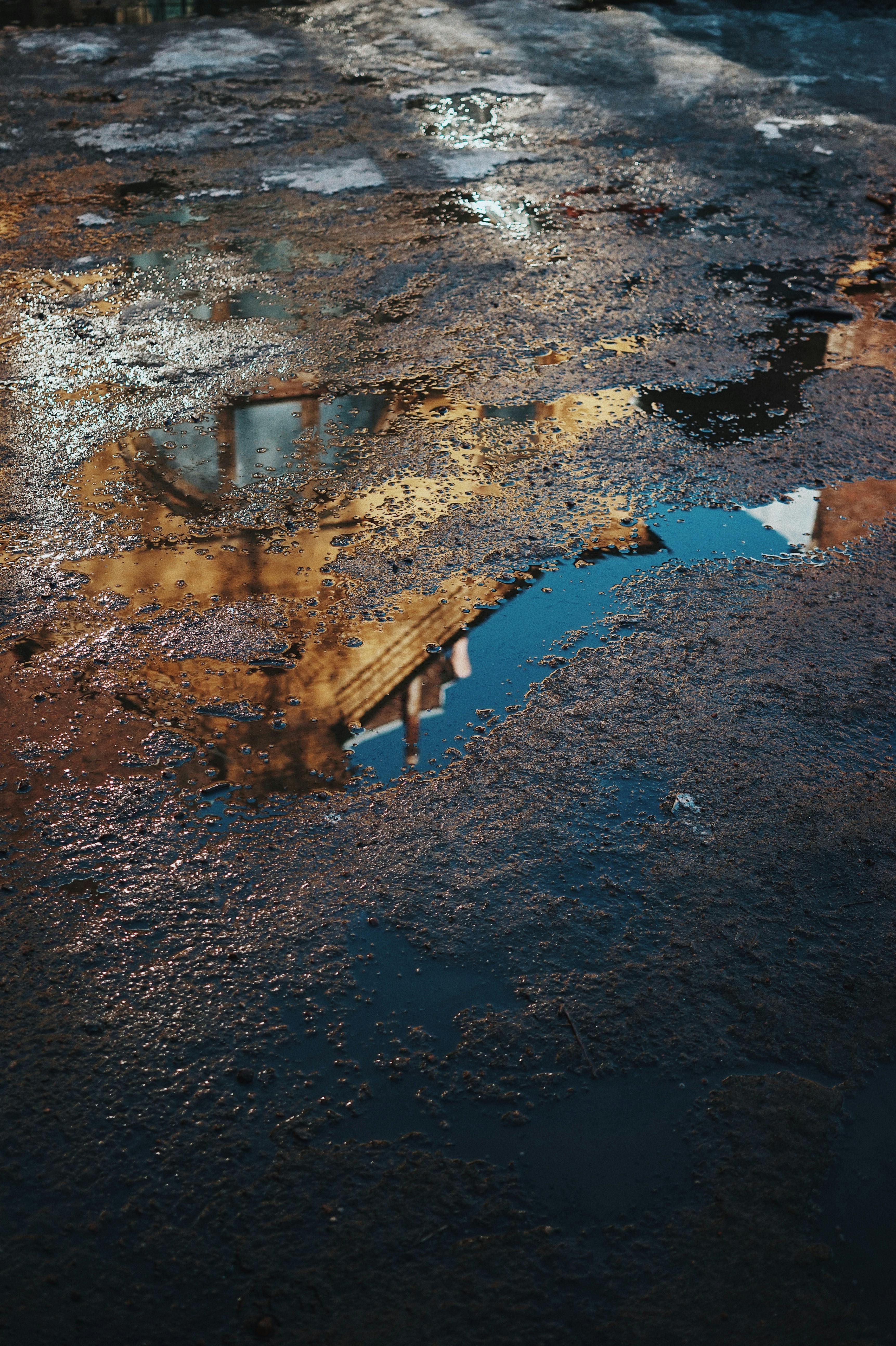 Puddle on urban ground reflecting a building at sunset, showcasing city texture.