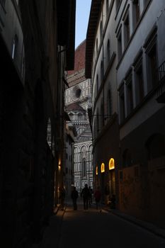 A shadowy alley in Florence revealing a glimpse of a historic cathedral at twilight.