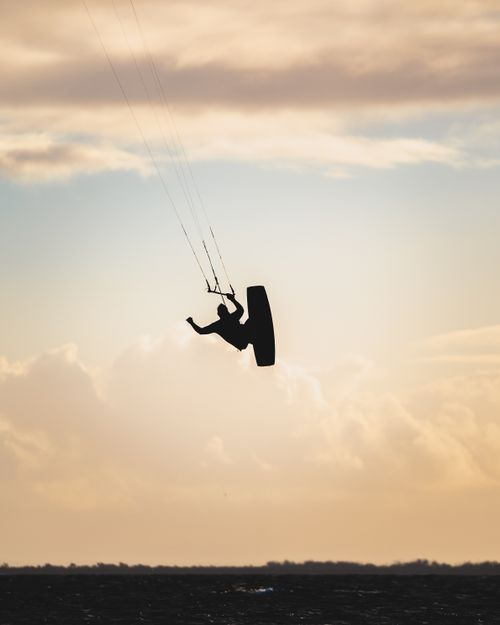 Free A dynamic silhouette of a kiteboarder jumping high against a dramatic sunset sky, capturing the essence of adventure and freedom. Stock Photo
