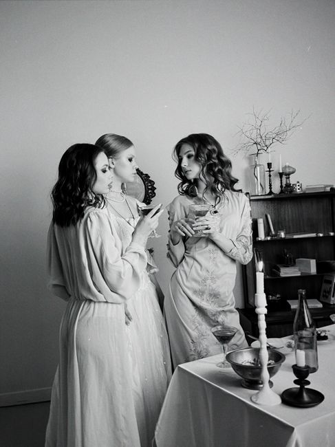 Three women in vintage dresses enjoying an elegant evening socializing and sipping wine.