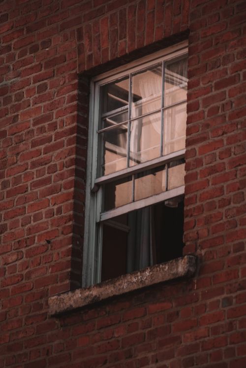 Free A rustic brick building featuring an open window reflecting the urban exterior. Stock Photo