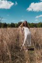 Woman in White Dress Standing on Brown Grass Field Under Blue Sky