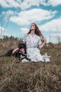 Woman in White Dress Sitting on Brown Grass Field Beside Black Short Coated Dog