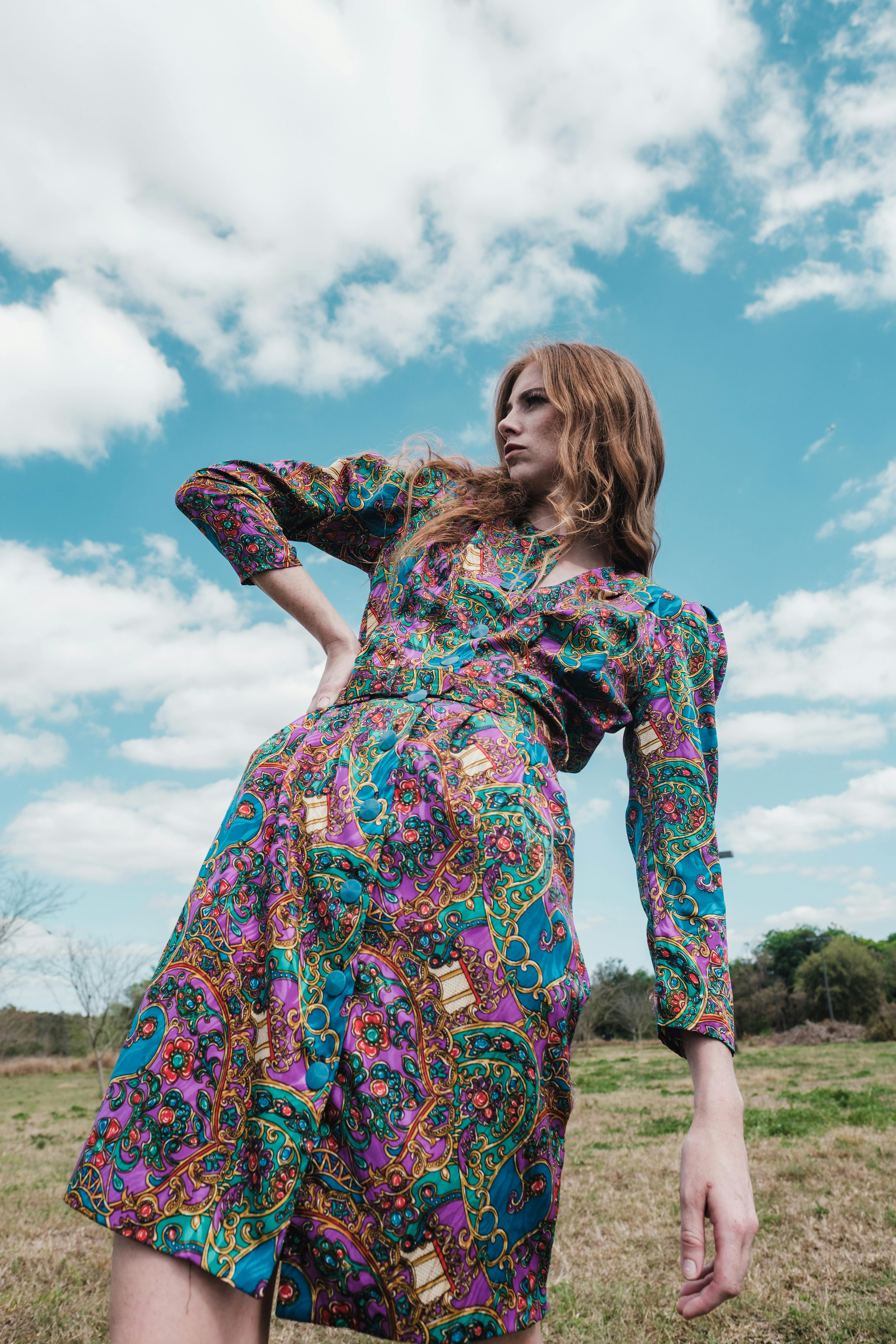 Stylish model poses confidently in a vibrant floral dress under a bright sky.