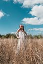 Woman in White Sleeveless Dress Standing on Brown Grass Field Under Blue Sky