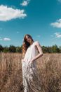 Woman in White Sleeveless Dress Standing on Brown Grass Field Under Blue Sky