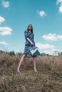 Woman in Black and White Floral Dress Standing on Green Grass Field Under Blue Sky during