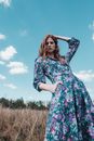 Woman in Blue and Red Floral Dress Standing on Green Grass Field