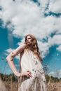 Woman in White Sleeveless Dress Standing on Green Grass Field Under Blue Sky and White Clouds