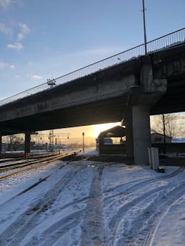A snow-covered bridge and train tracks at sunrise in winter, highlighting urban infrastructure.