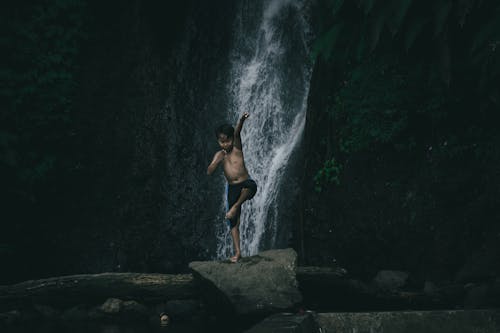 Child standing on a Boulder near Waterfalls in One Leg 