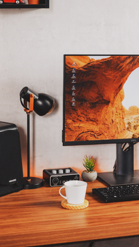 Stylish home office workspace with monitor, lamp, and coffee cup on a wooden desk.