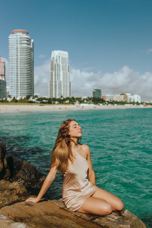 Woman Sitting on Rock on Coast Near City