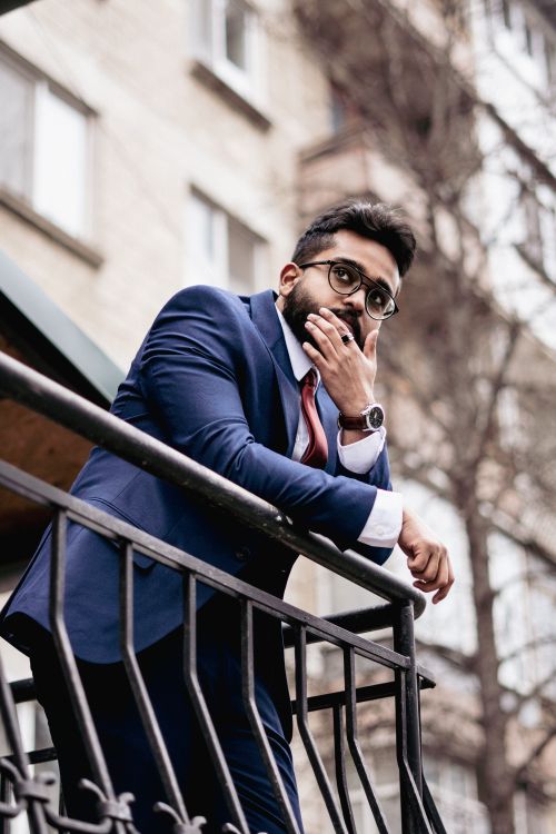 Free Confident businessman in a blue suit standing on a balcony in an urban environment, gazing thoughtfully ahead. Stock Photo