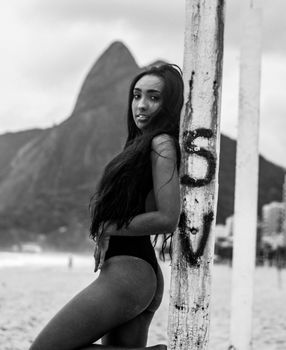 Monochrome portrait of a woman in swimwear at a beach, featuring a mountain view.