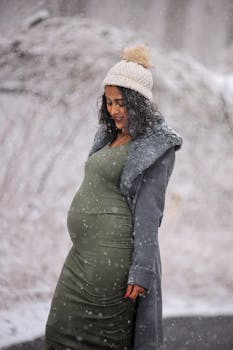 Beautiful pregnant woman smiling outdoors in a snowy winter landscape, wearing a cozy winter outfit.