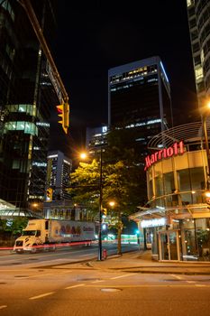 Vibrant nighttime city scene in downtown Vancouver featuring skyscrapers and a bustling street.