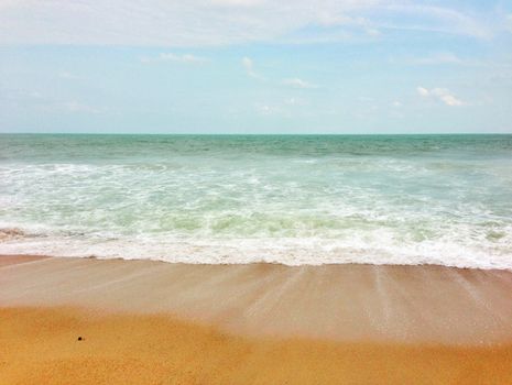 Serene beach with gentle waves under a bright blue sky, perfect for a peaceful getaway.