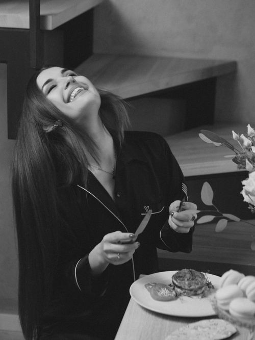 Free Woman laughing with a fork and knife at a dining table indoors. Grayscale photo. Stock Photo