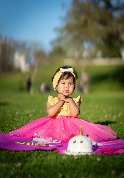 Free A Girl in Pink Dress Sitting on Green Grass Field Stock Photo