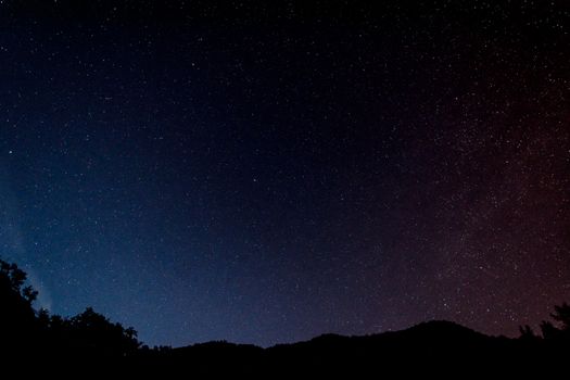 A serene view of a star-filled night sky over silhouettes of hills in Italy.
