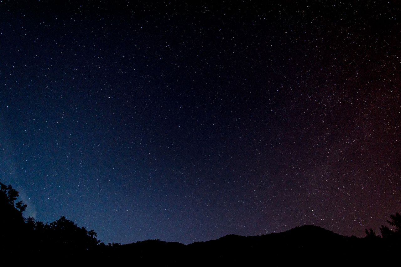 a serene view of a star filled night sky over silhouettes of hills in