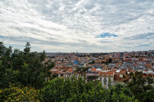 Free Explore the vibrant rooftops of Lisbon beneath a dramatic cloudscape. Perfect for travel and architecture enthusiasts. Stock Photo