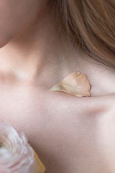 Close-up of a woman's collarbone with a soft petal, capturing elegance and natural beauty.