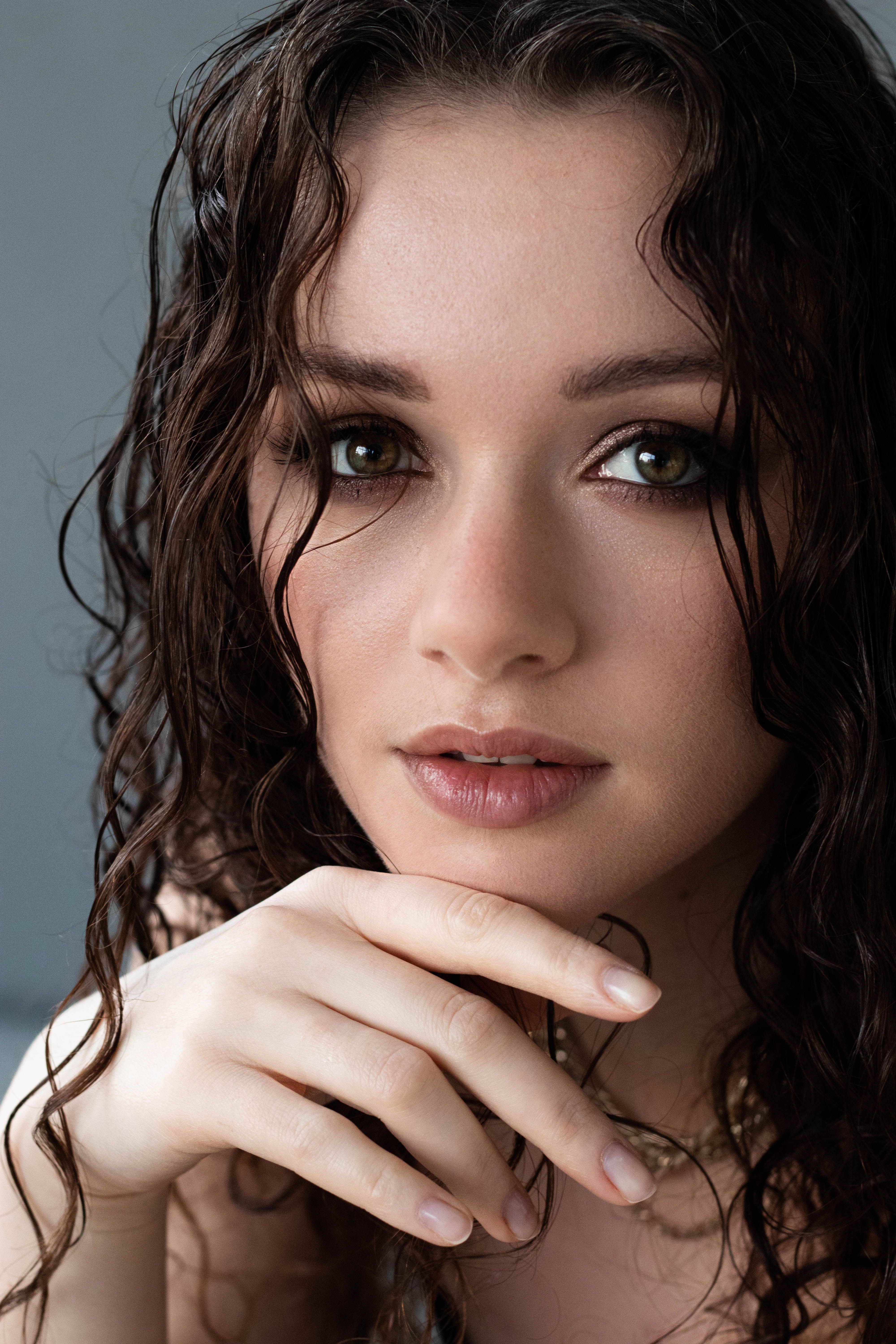 Close-up portrait of a woman with long wet hair and subtle makeup, exuding elegance.
